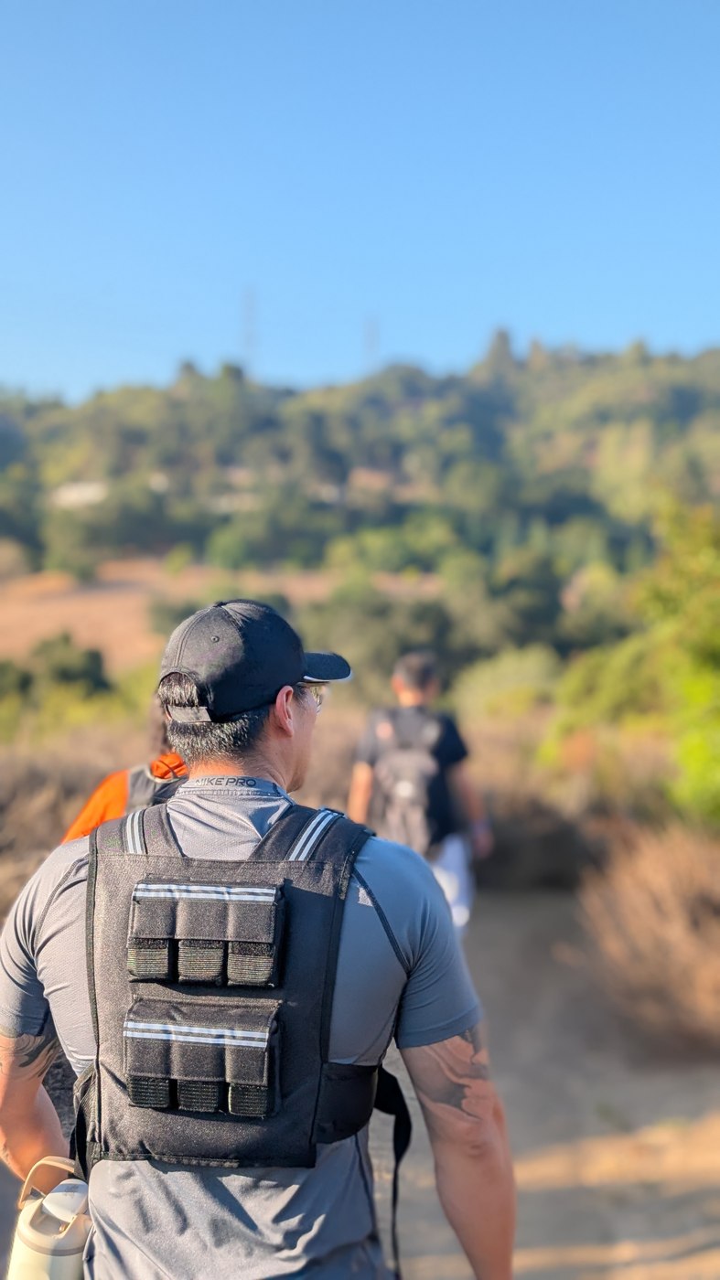 A person wearing a weighted vest walking on a sunlit trail.